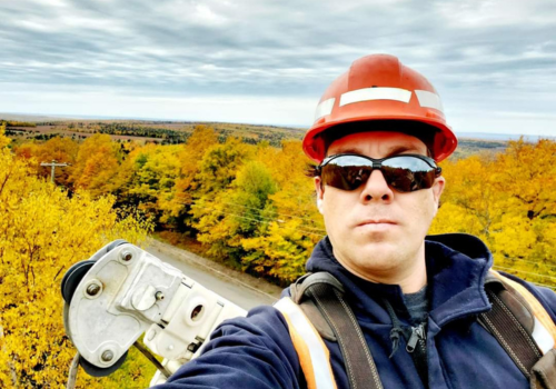 A utility worker named Aaron Leblanc, wearing a hard hat and sunglasses, capturing a selfie.