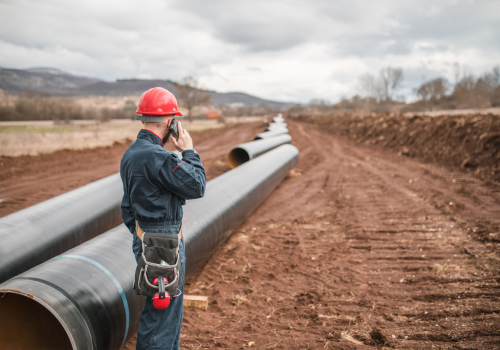 An engineer in a uniform and with a helmet on his head uses a mobile phone while controlling the operation of the gas pipeline